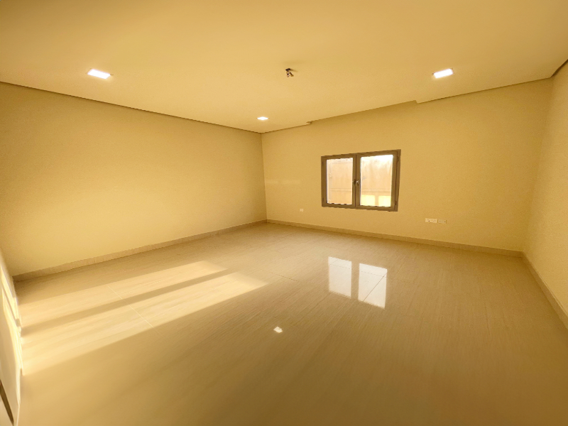 Empty room with cream-colored walls, a window on the right wall, reflective tiled floor, and ceiling lights.