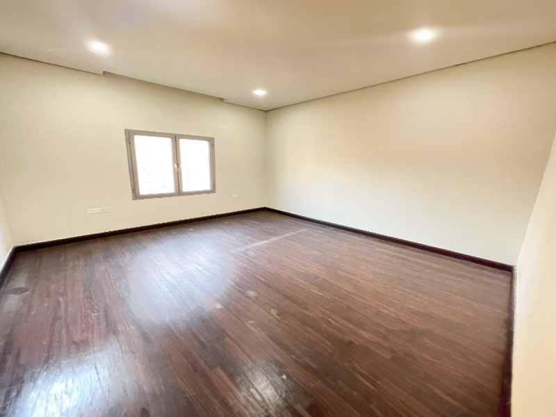 Empty room with wooden floor, white walls, and a single window, illuminated by ceiling lights.