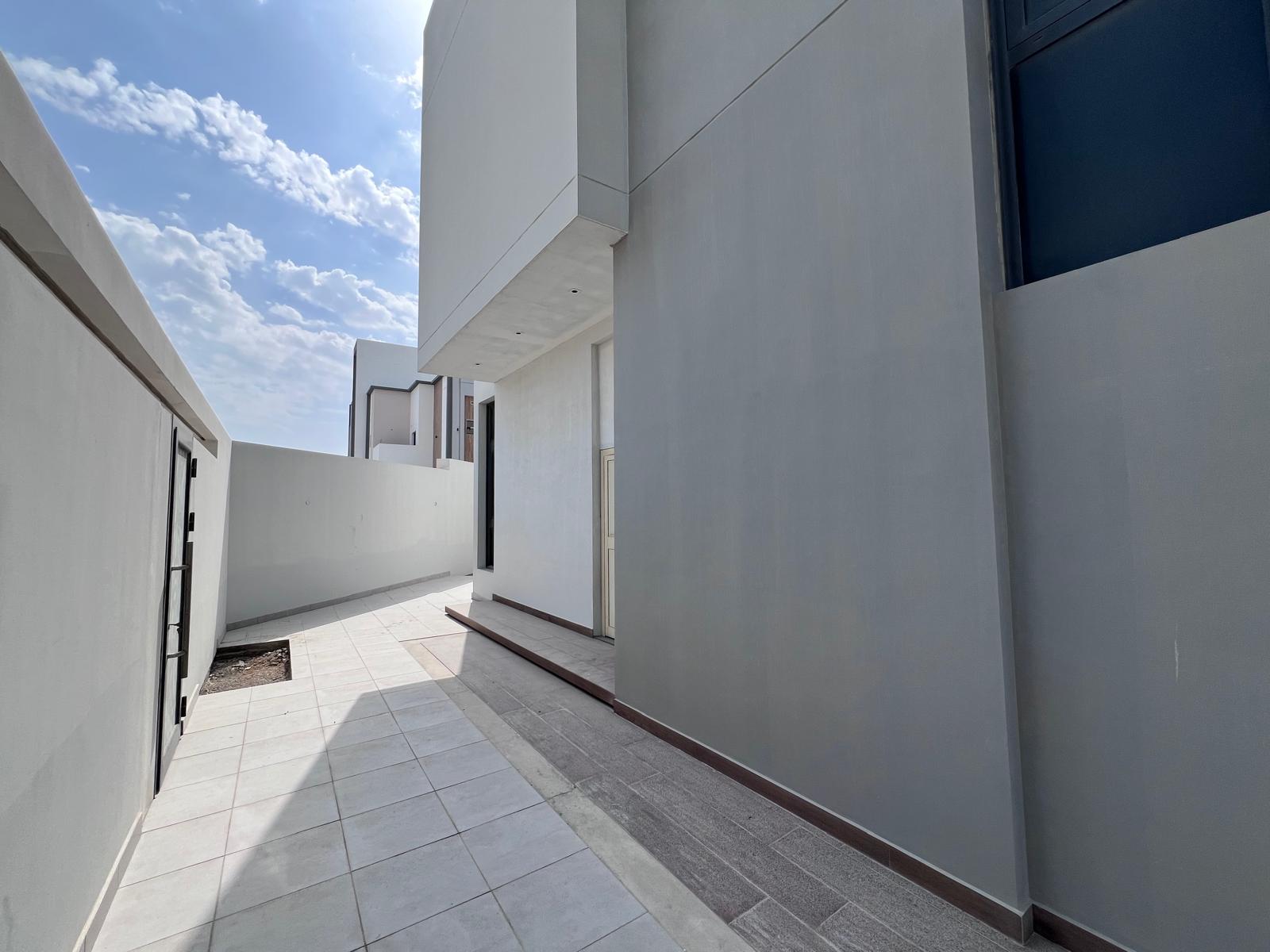 Narrow outdoor walkway between modern white buildings under a blue sky with clouds.