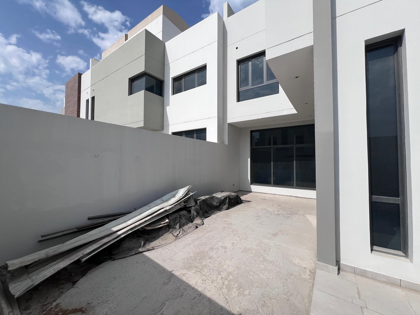 A modern white building with large windows and a concrete backyard. Construction materials are stacked on the ground.