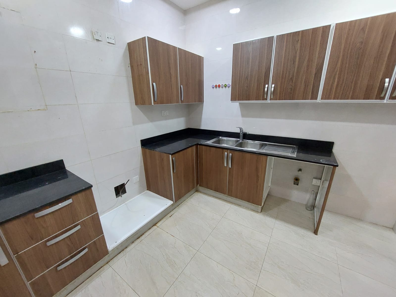 Kitchen with wooden cabinets, dark countertops, stainless steel sink, and white tiled walls and floor.