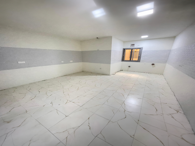 Empty room with tiled floor and white walls, featuring a small window on one side and overhead lights.