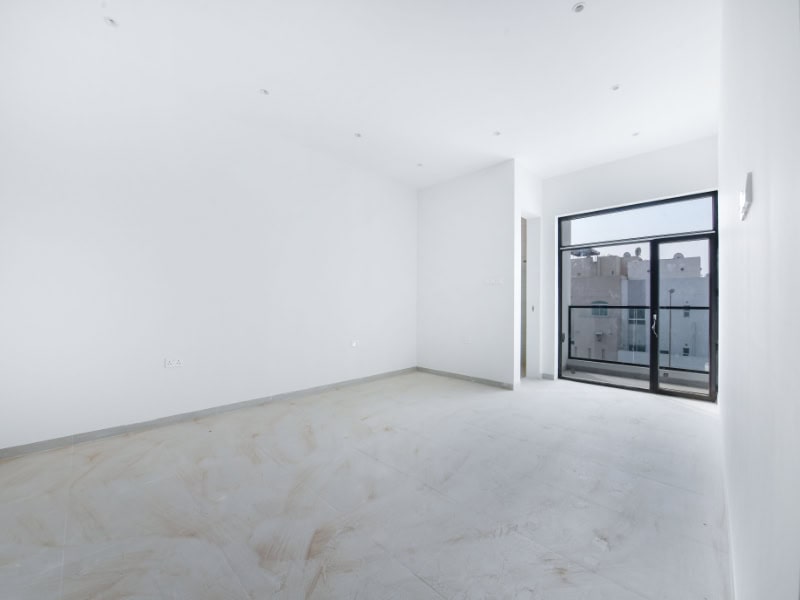 An empty, unfurnished room with white walls and tiled floor, featuring a large window with a view of building exteriors.