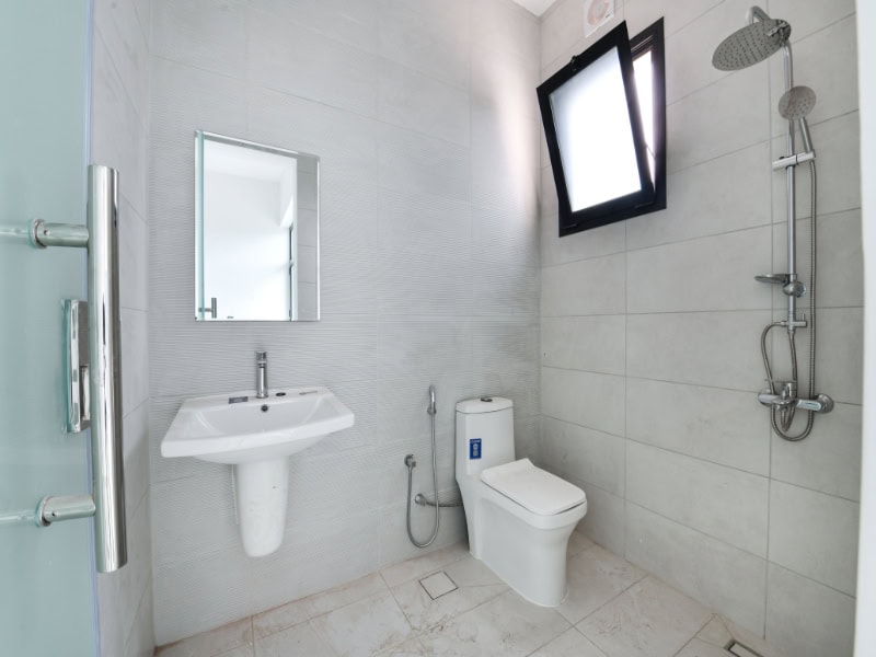 Modern bathroom with a wall-mounted sink, mirror, and toilet. A shower area is on the right with a wall-mounted showerhead. Walls and floor are tiled in light gray.