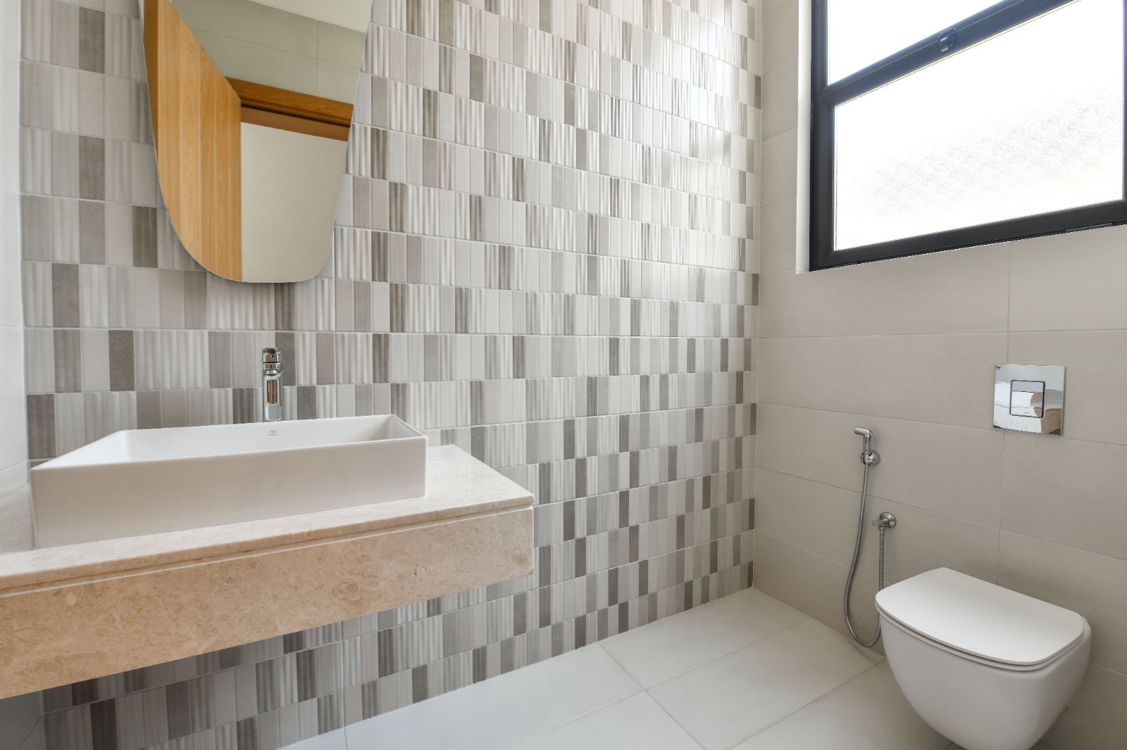 Modern bathroom with a wall-mounted sink, geometric tile wall, wall-mounted toilet, and a large frosted window.