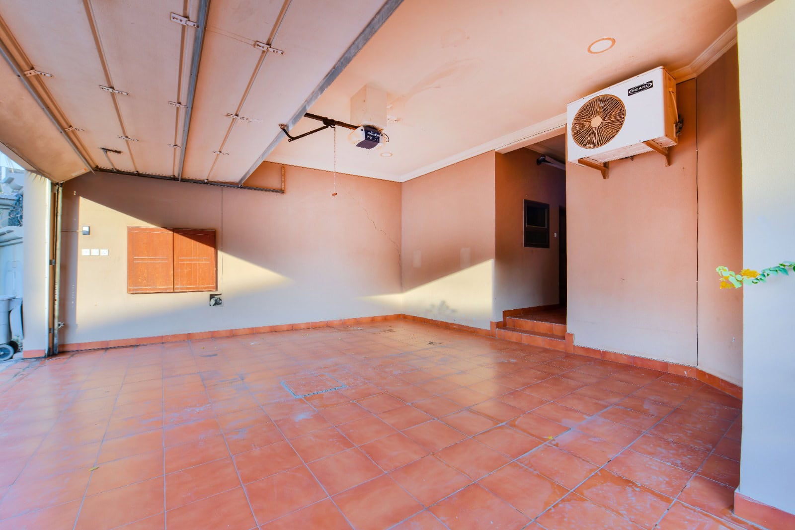 Empty garage with a tiled floor, beige walls, and an overhead door. An air conditioning unit is mounted on the wall.