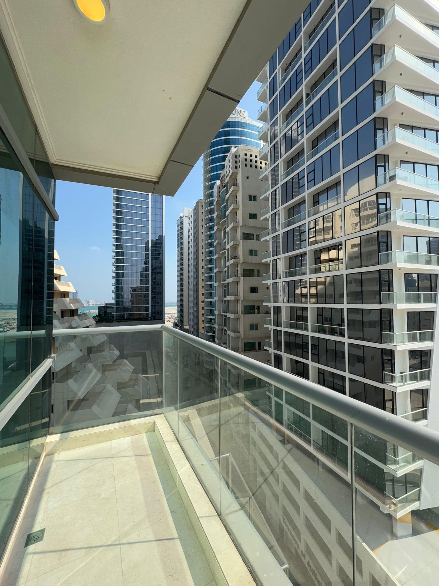 City view from a balcony with glass railings, surrounded by tall modern buildings under a clear blue sky.