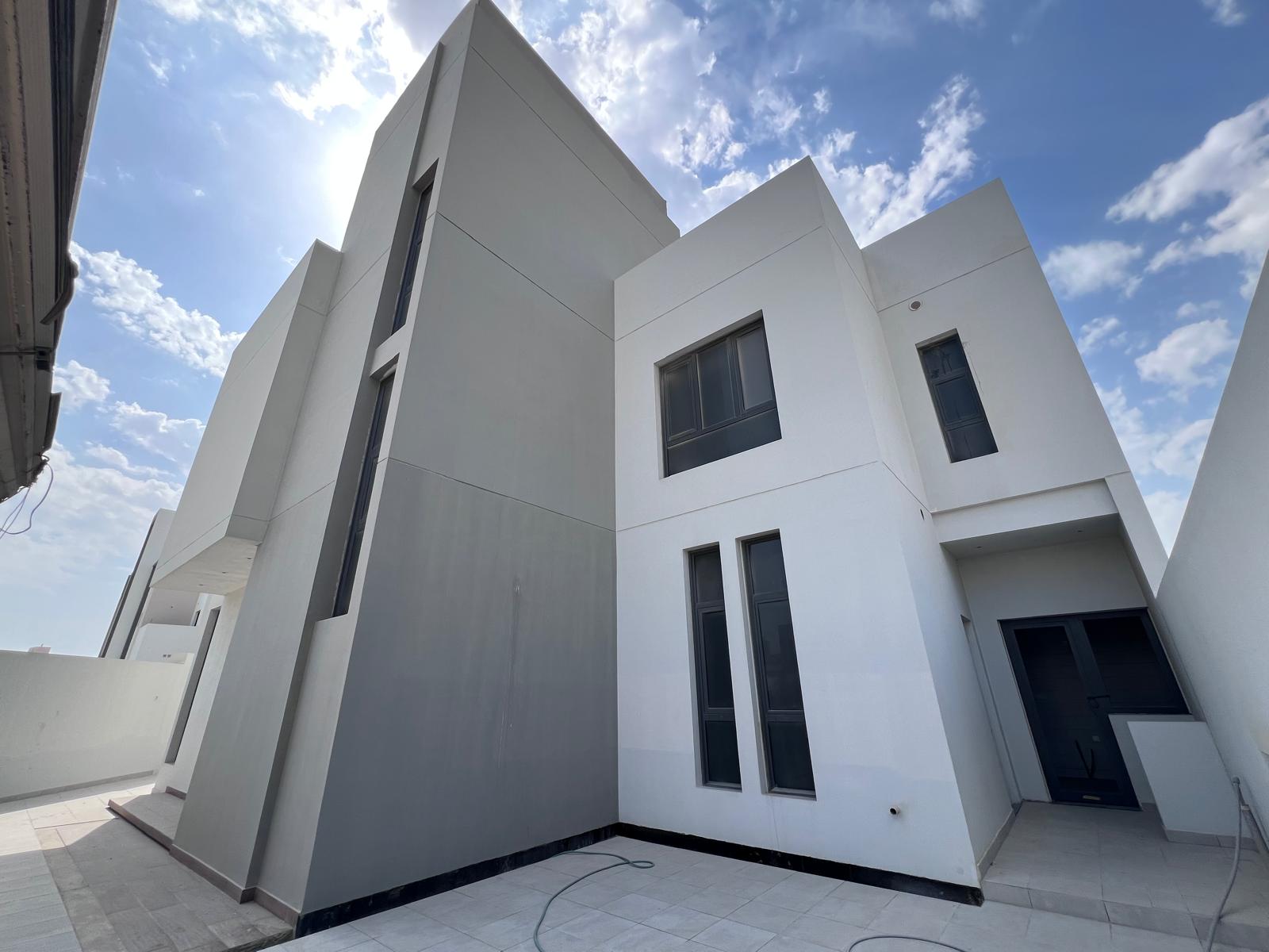 Modern multi-story building with minimalist design, featuring large windows and geometric shapes, under a partly cloudy sky.