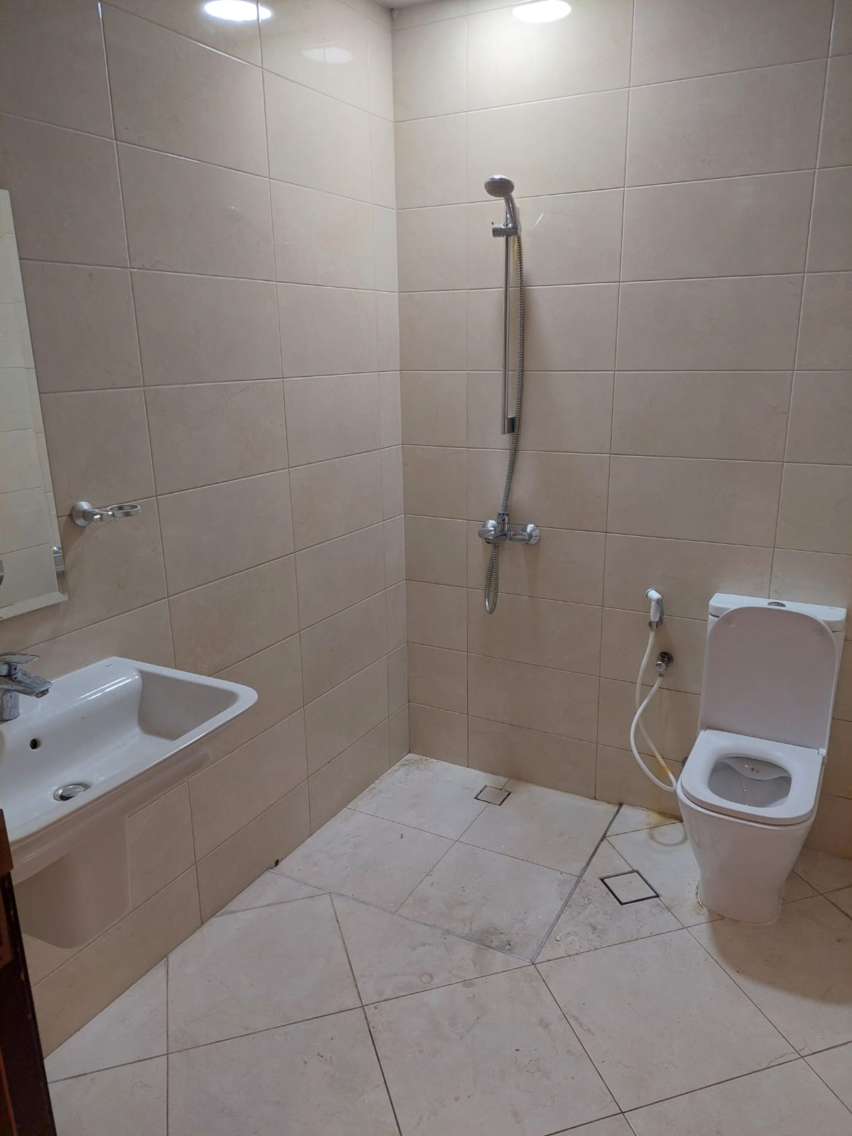 Bathroom with beige tiles, featuring a sink, a mounted mirror, a shower head, and a toilet.