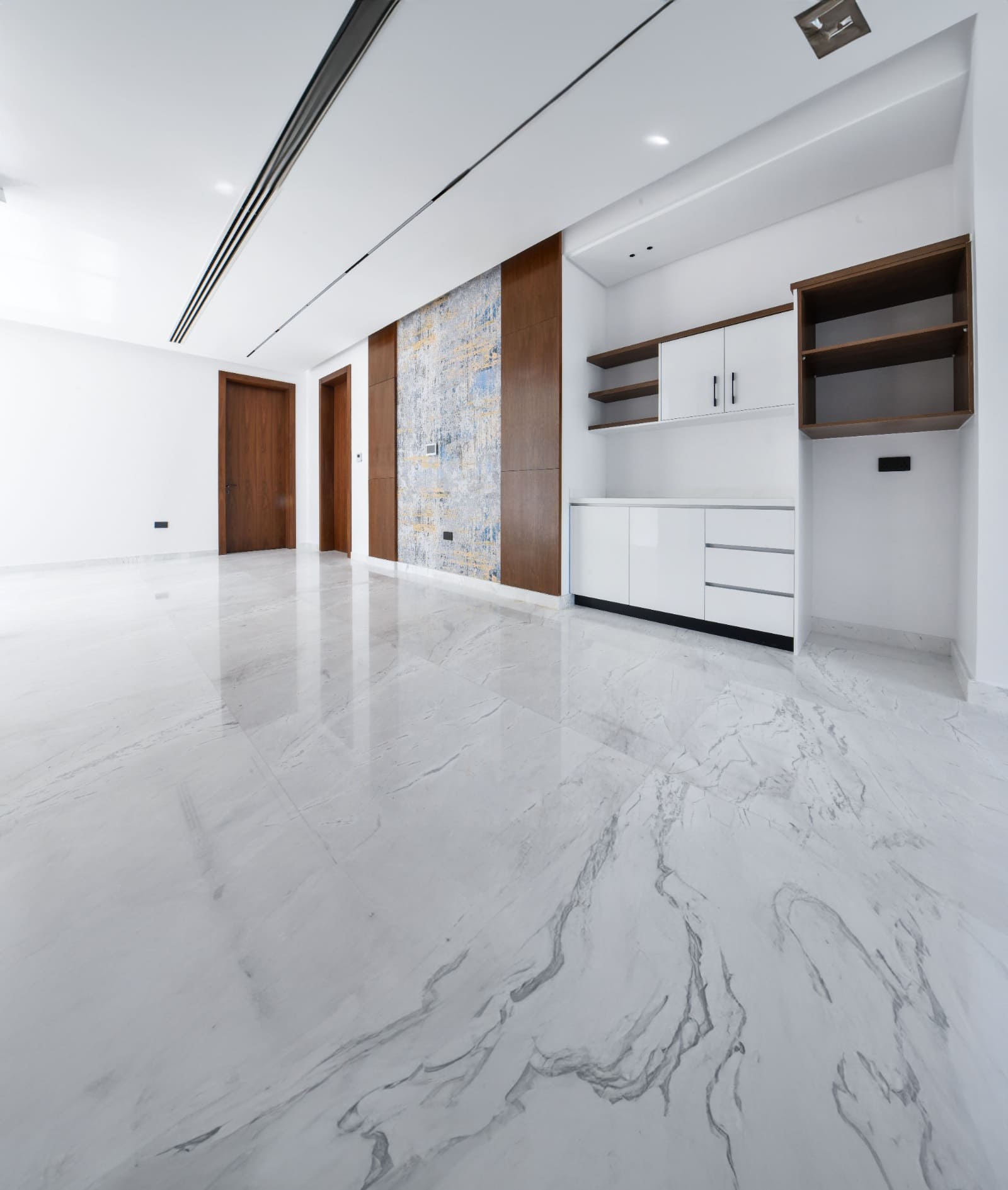 Spacious modern room with white marble floor, wooden panel accents, and built-in shelving units on a white wall.