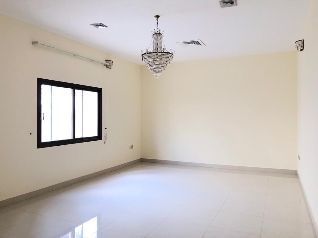 A vacant room with white walls, a large window with a black frame, a modern chandelier, and white tiled flooring.