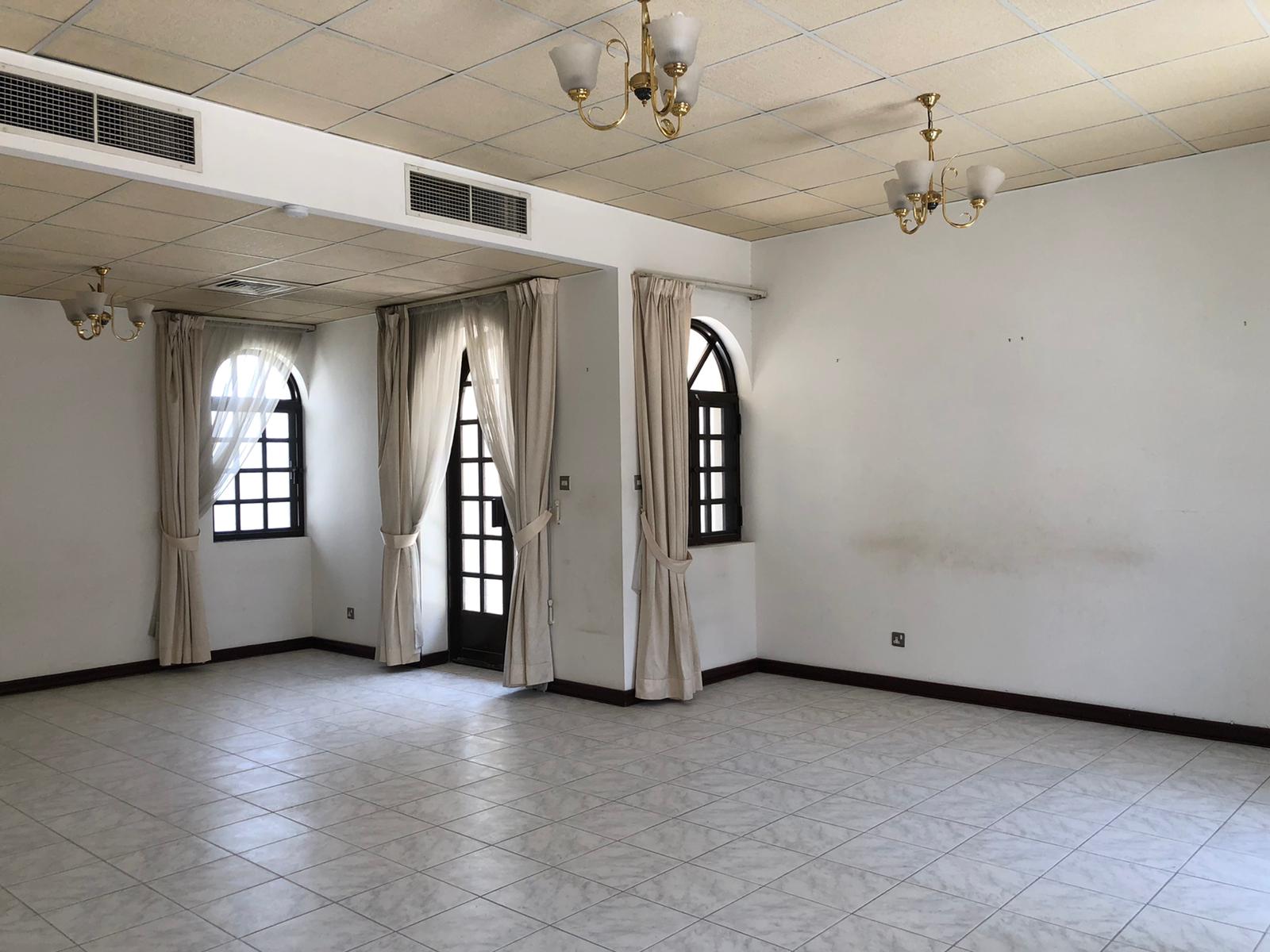 An empty room with tiled flooring, arched windows with curtains, ceiling lights, and a partial view of an air conditioning duct.