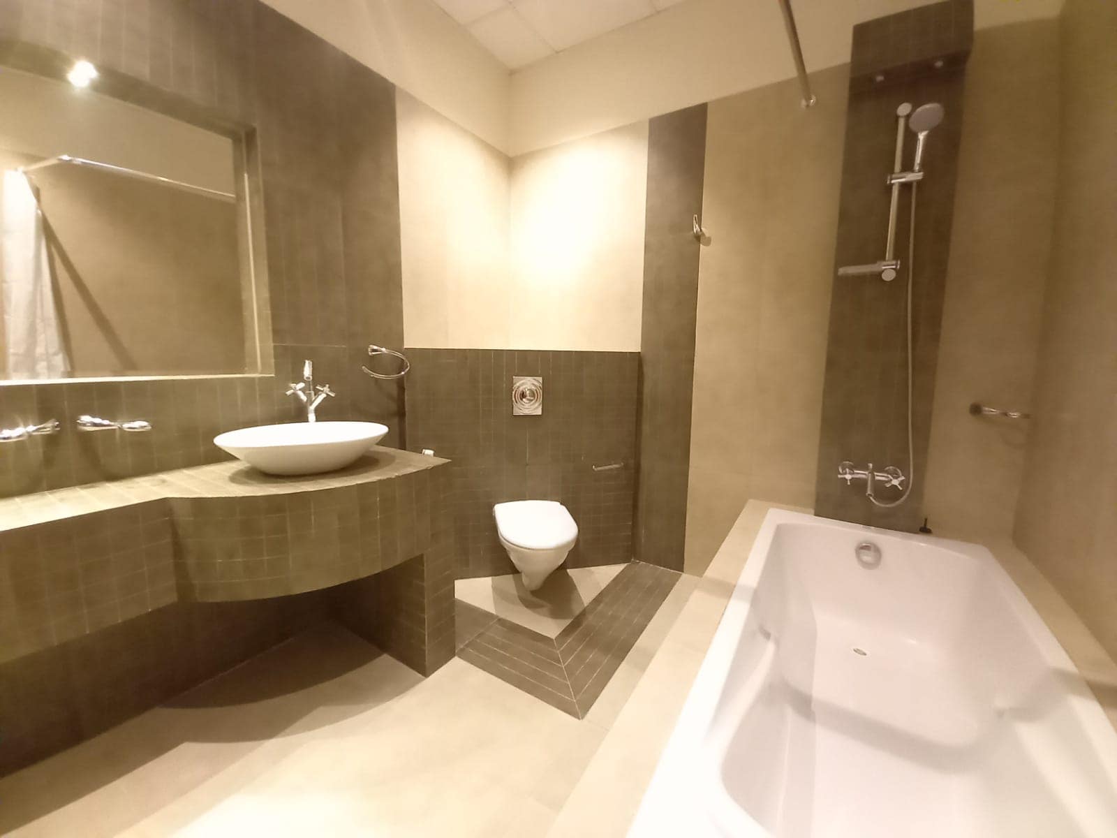 A modern bathroom with a bathtub, wall-mounted toilet, floating sink, large mirror, and tiled walls.